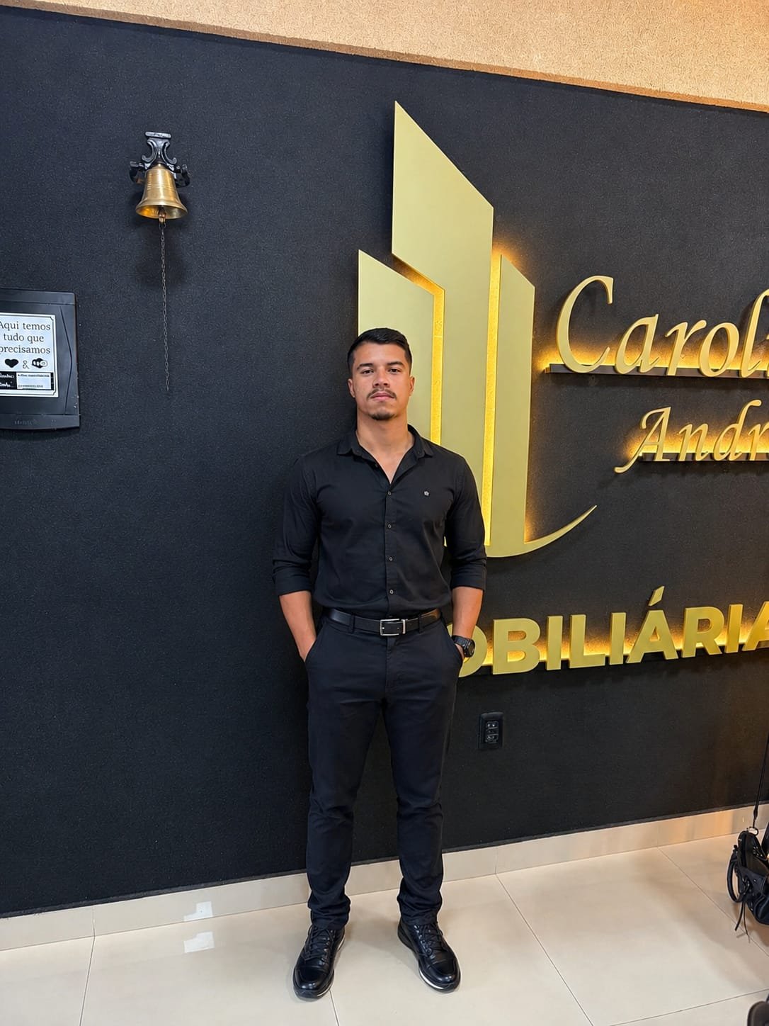 Lucas Matheus em frente à identidade visual da Carolina e Andrade Imóveis